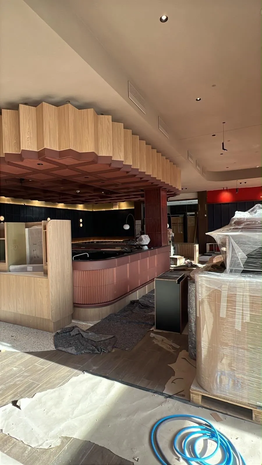Een horecazaak in aanbouw, met een ronde bar, een houten lamellenplafond en meubels nog onder folie
